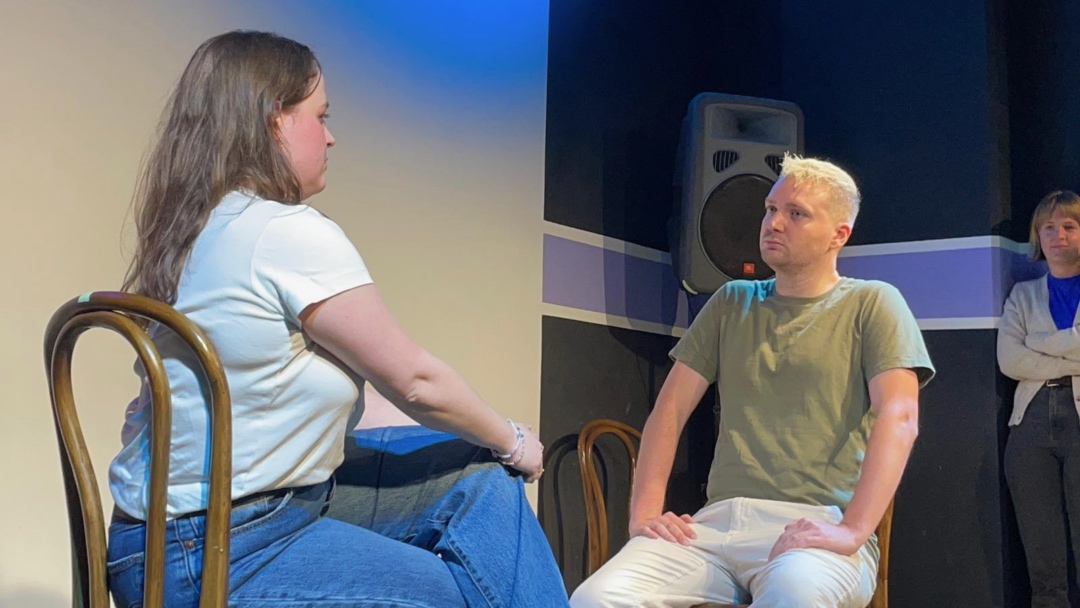 Max is sitting on a chair opposite his scene partner on the stage at Improv Theatre Sydney.