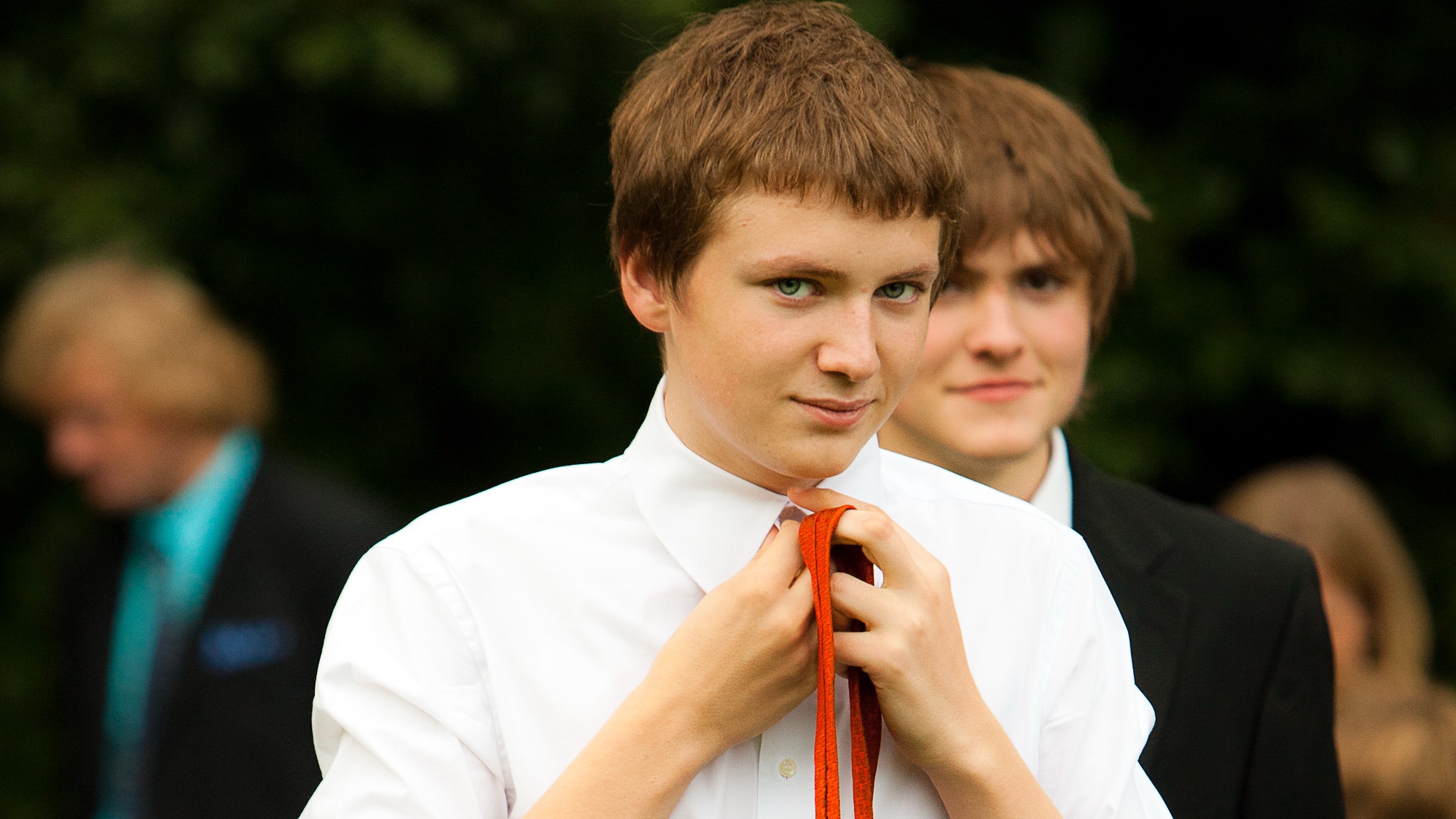 A photograph of a 16 year old Max, with a 16 year old Peter in the background. Both wearing suits