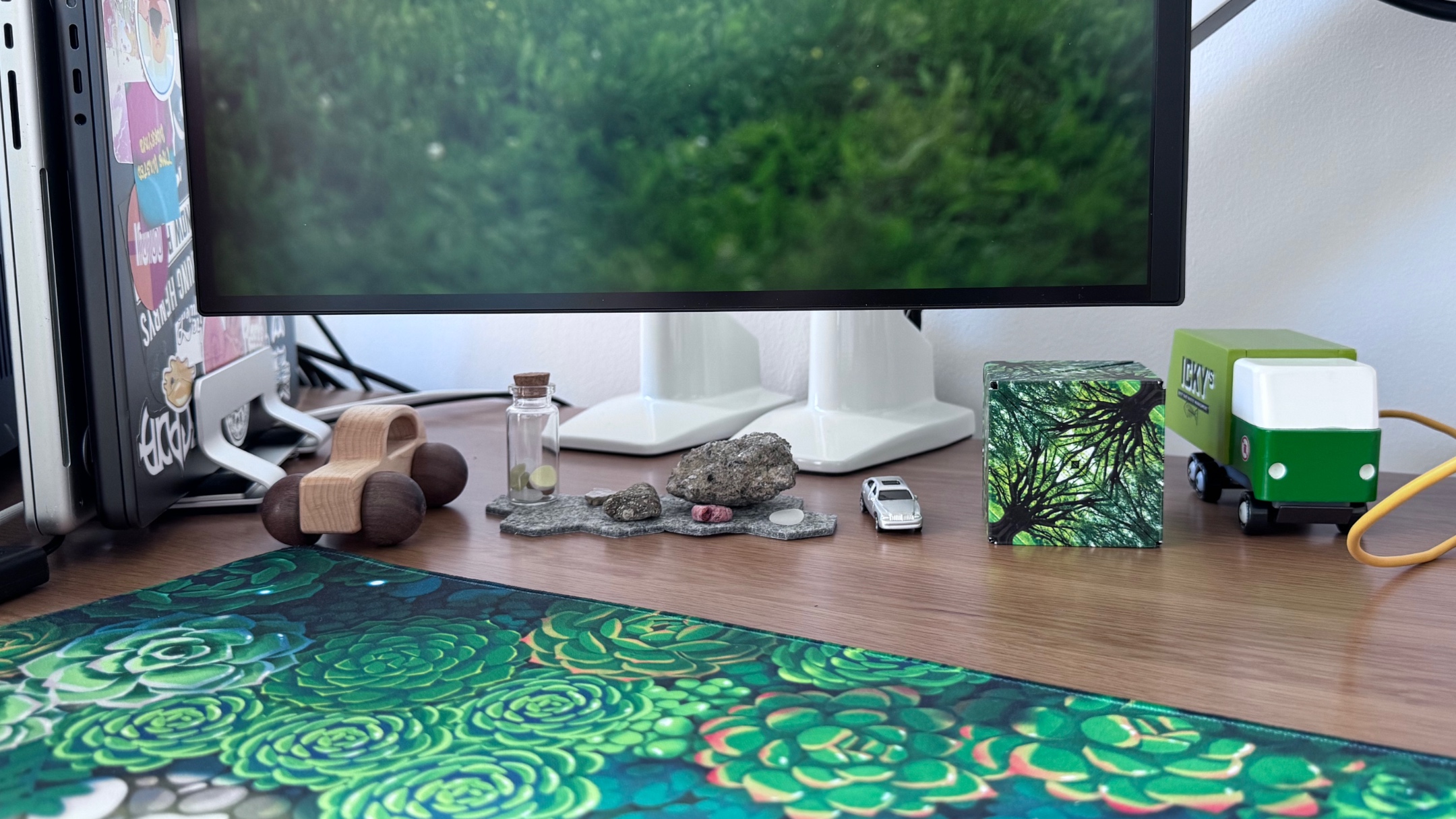 A photograph of some rocks and sea glass, as well as some wooden toy vehicles, collected under a monitor